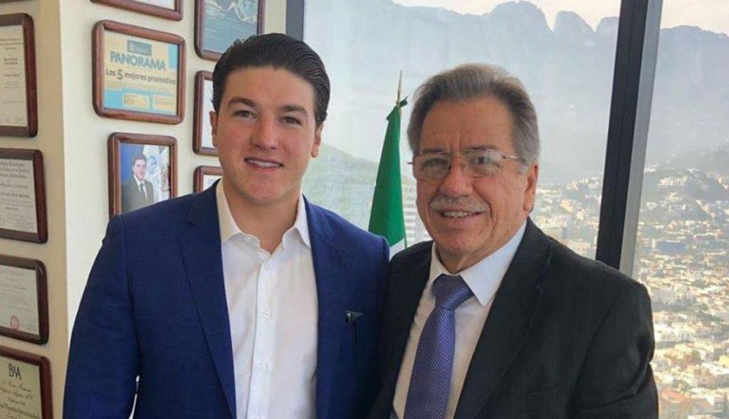Two Men in Suits Posing for a Photo in a Bright Office, with Framed Certificates on the Wall and a Mexican Flag in the Background. - Alcaldes Regios