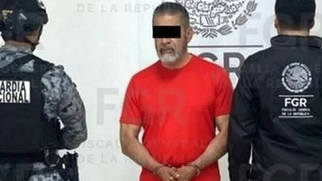 La-empresa-maquiladora-de-lubricantes-pago-millones - Alcaldes Regios Arrest Scene: Man in a Red Shirt Handcuffed Between Two Officers in Tactical Gear, Eyes Obscured by a Black Bar; Police Backdrop Behind Them. - Alcaldes Regios